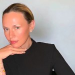 A white woman with dark blonde hair wearing a black long-sleeve top, looks at the camera.