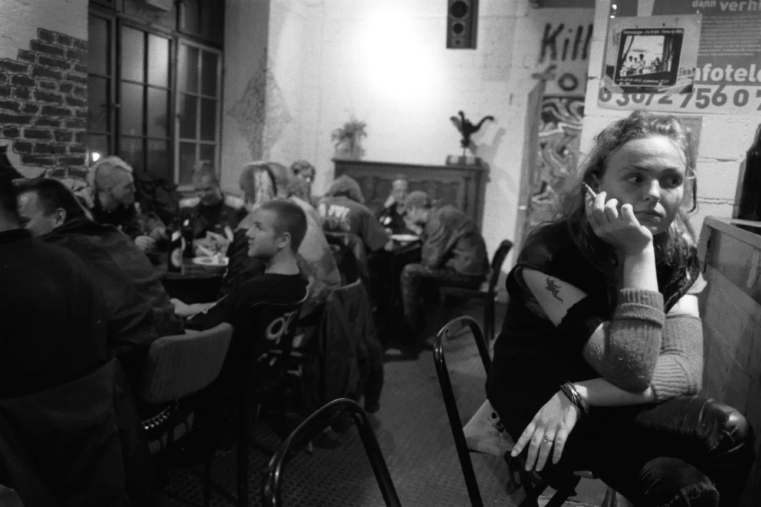 A girls sits at the bar smoking with other young people behind her seated at tables.