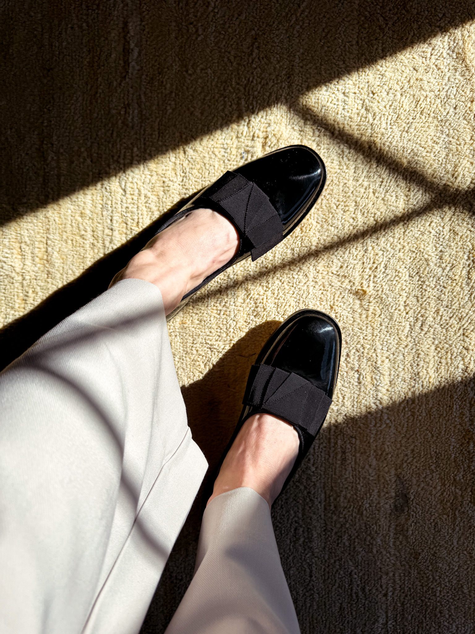 An overhead shot of a woman's feet wearing black flats with black bows on top