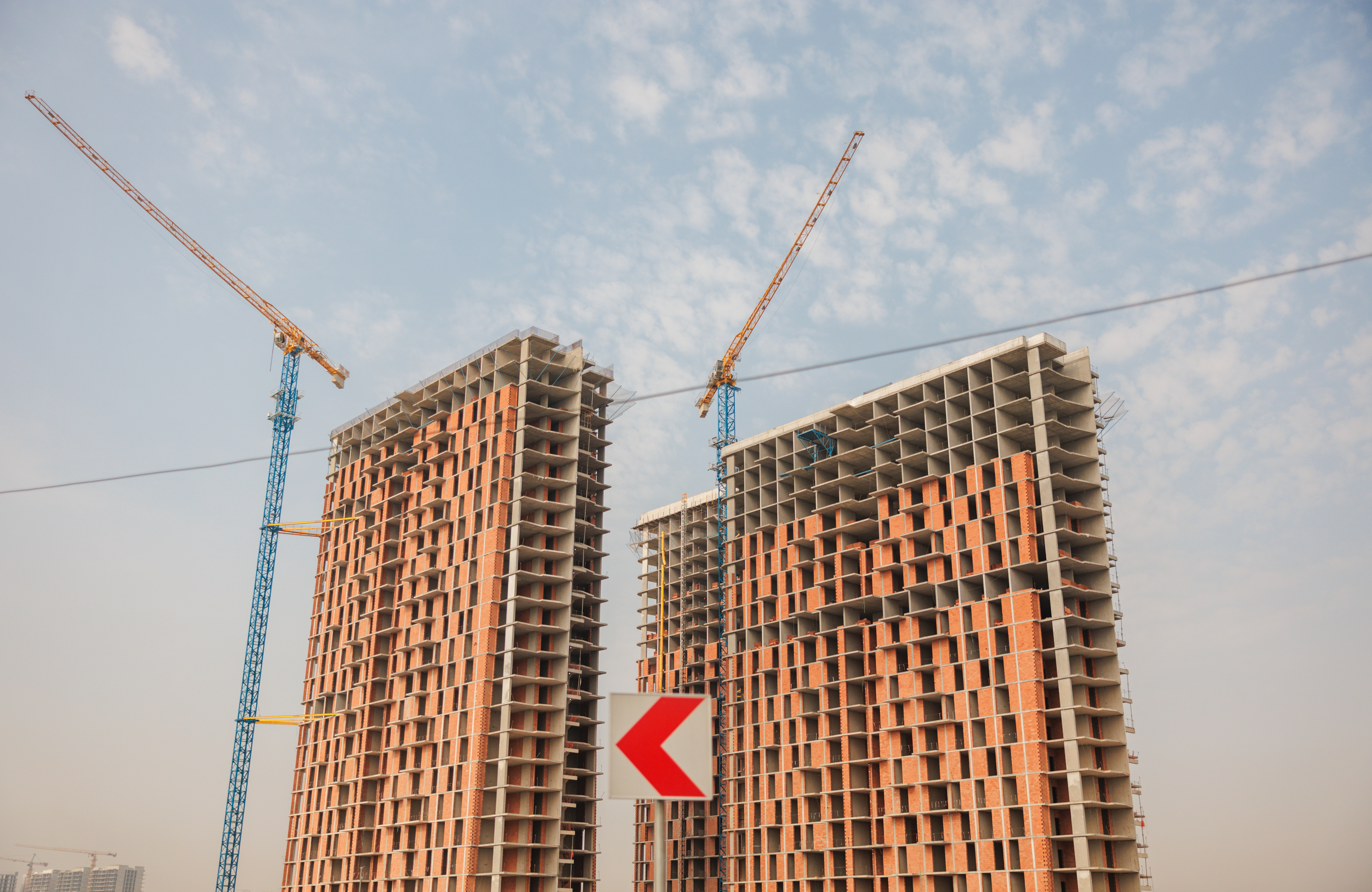 Construction cranes and two or three high rise buildings under construction against a blue sky.