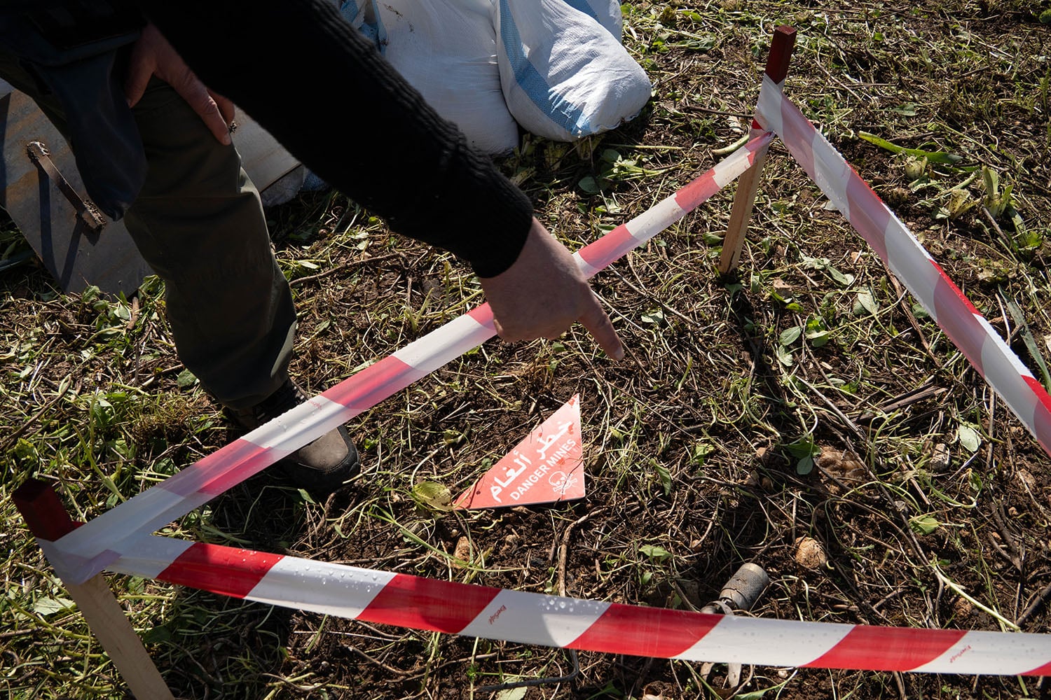 A triangle of striped tape marks off an area as a hand from a person out of frame points toward it.