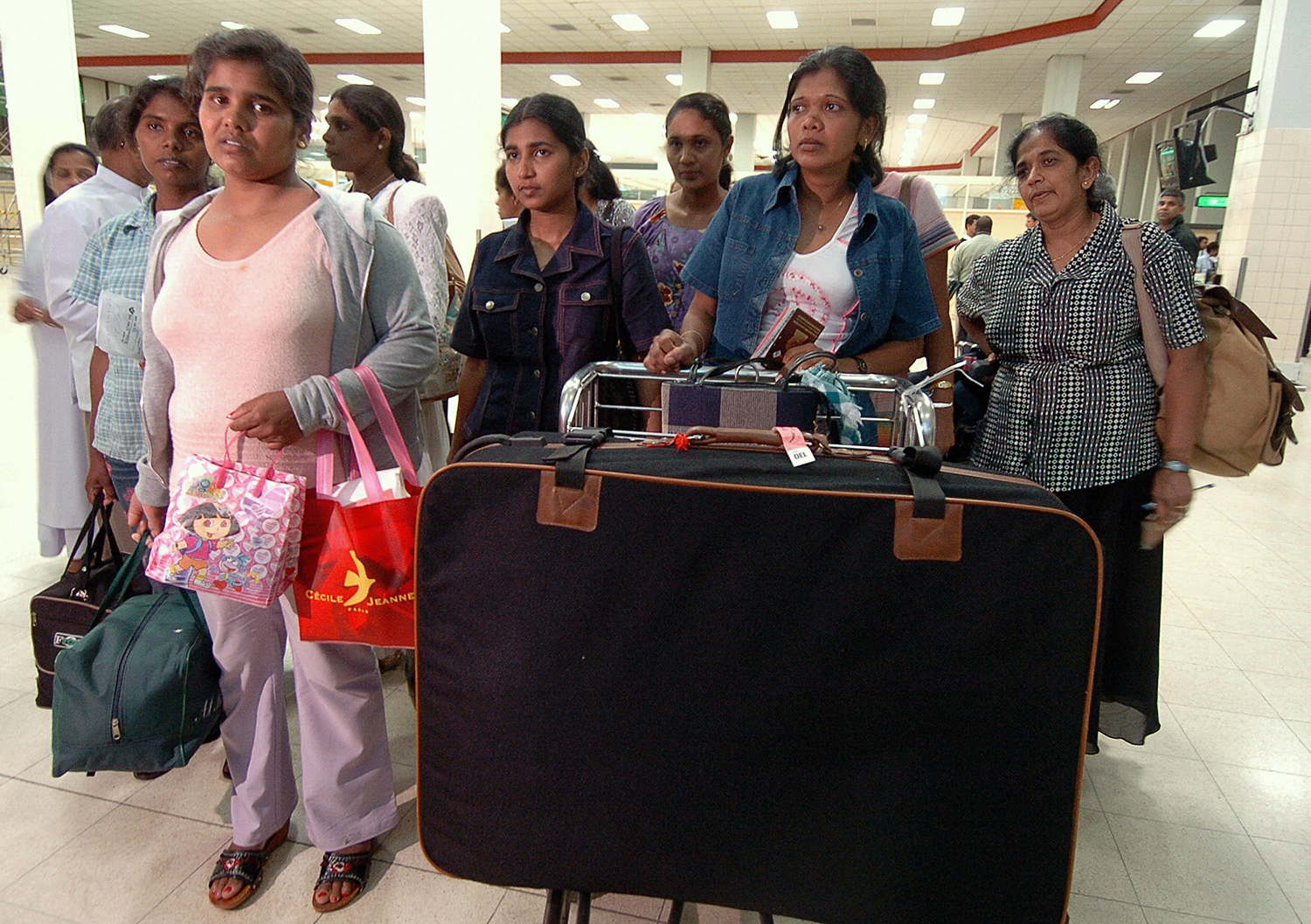 Several women carry bags and stand behind a large suitcase.