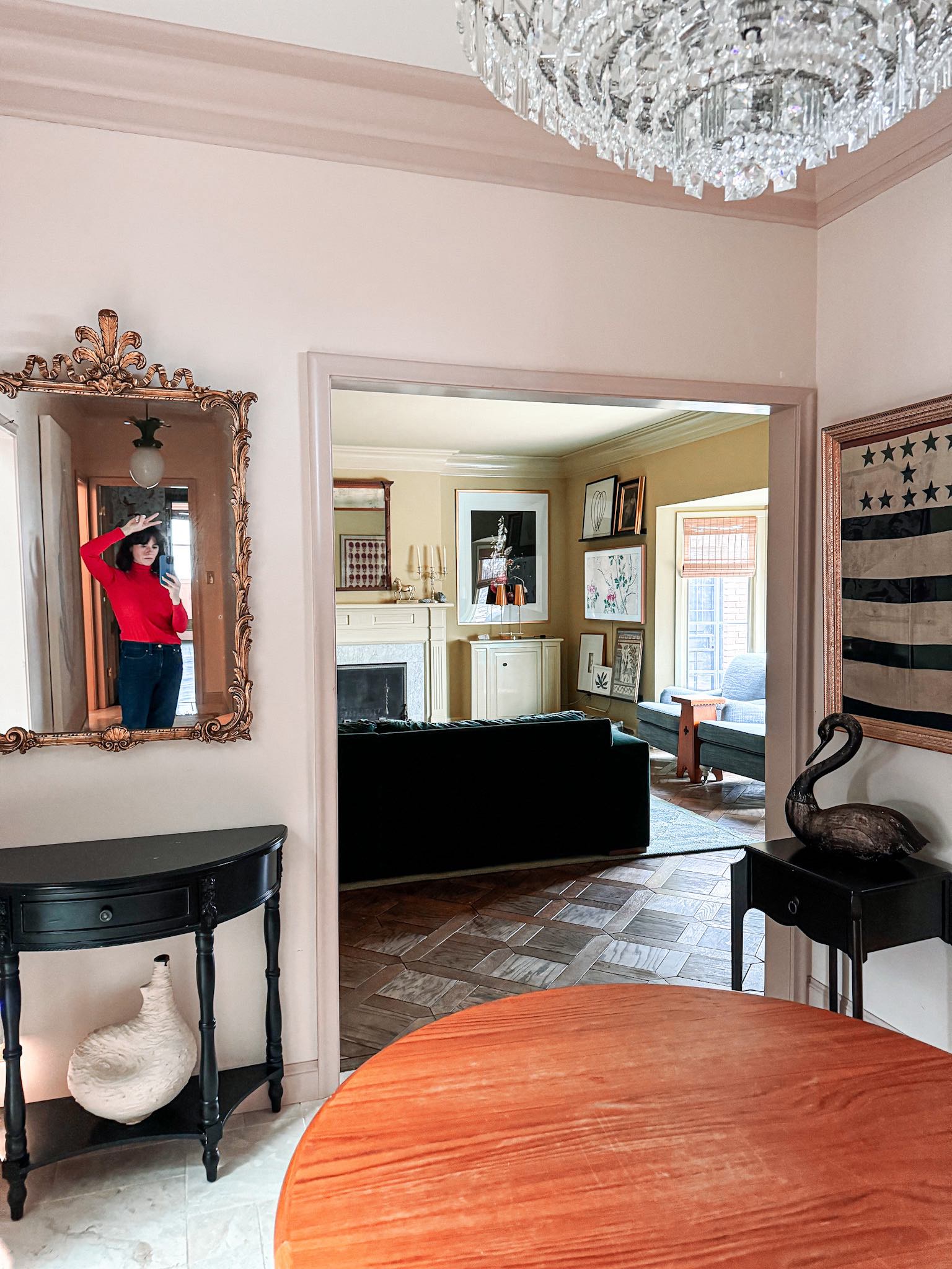 A woman is shown in a mirror in her entryway with a green-painted family room in the background