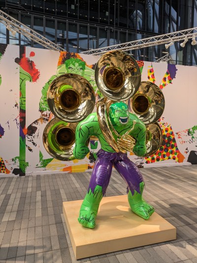 A sculpture consisting of an inflatable  green Hulk that has five tuba heads attached to it. 