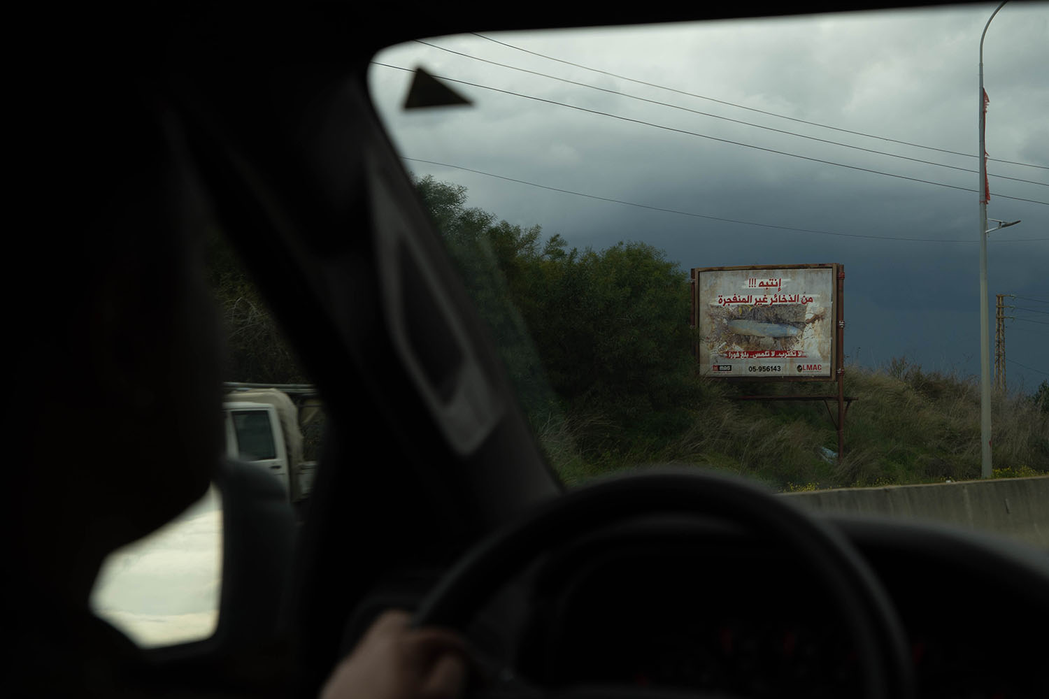 A roadside sign is seen through the window of a car with a driver at the wheel.