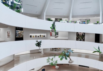 A rotunda whose ramps are filled with paintings. In the center, there are plants that are tied to the ceiling.