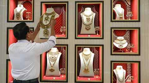 An employee arranges a gold necklace on a mannequin inside a display case at a jewellery store.