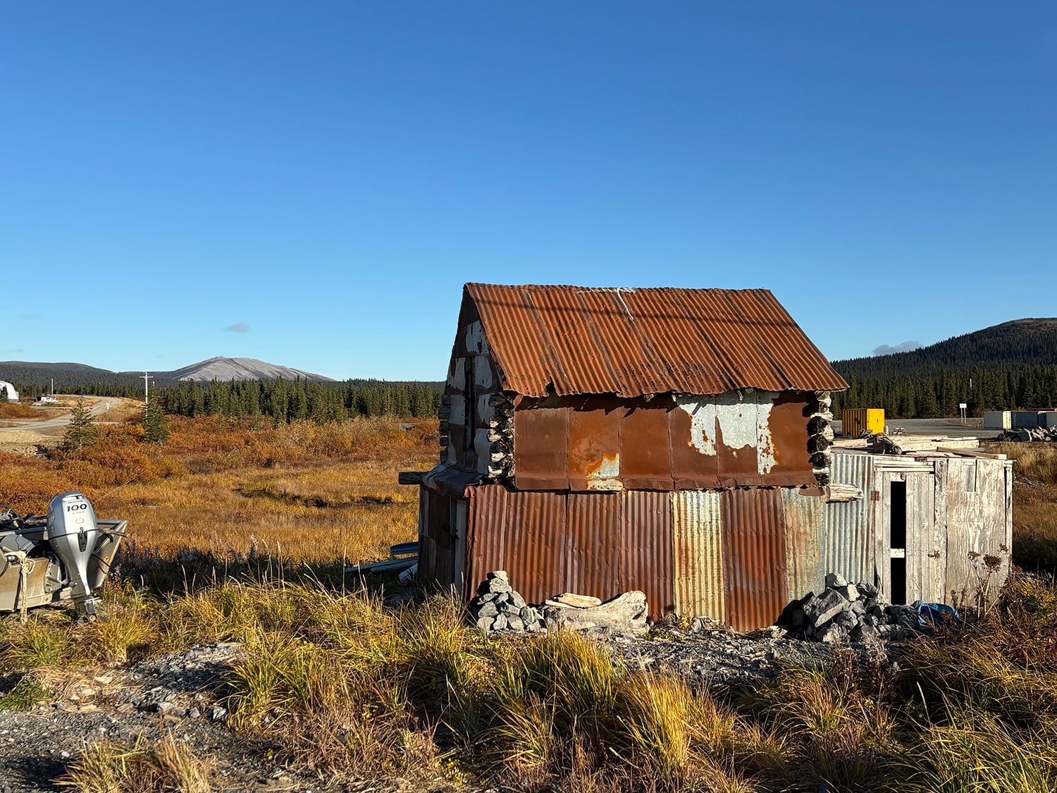 A ramshackle building with a rusted, corrugated roof in a field against a blue sky.