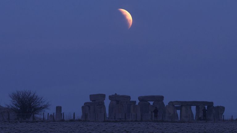 People view the full moon as a section moves into shadow during a lunar eclipse, before dawn, at Stonehenge stone circle, near Amesbury, southern Britain, March 14, 2025. REUTERS/Toby Melville