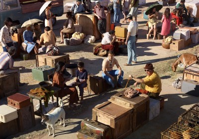 A photograph of people and animals sitting on boxes amid suitcases. Some people hold umbrellas.