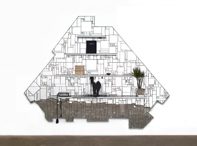 An artwork composed of unevenly sized glass panels. There are shelving unites attached that hold books and plants.