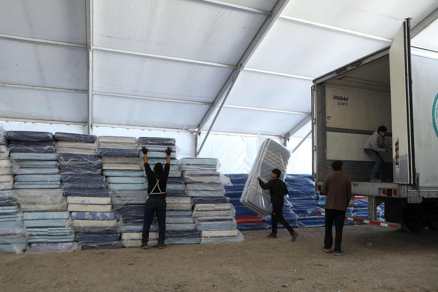 Workers unload dozens of mattresses from a truck at a temporary shelter.