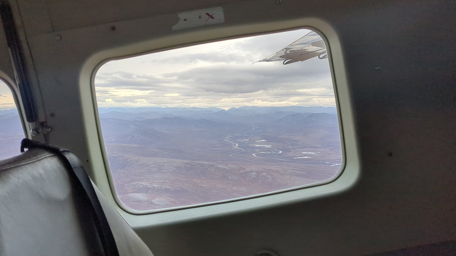 A view of mountains, rivers, and land out the window of a small plane.
