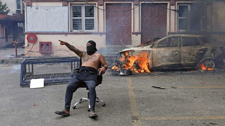 A demonstrator sits on a chair next to a burning car at the Supreme Court during this week's disorder. Pic: Reuters