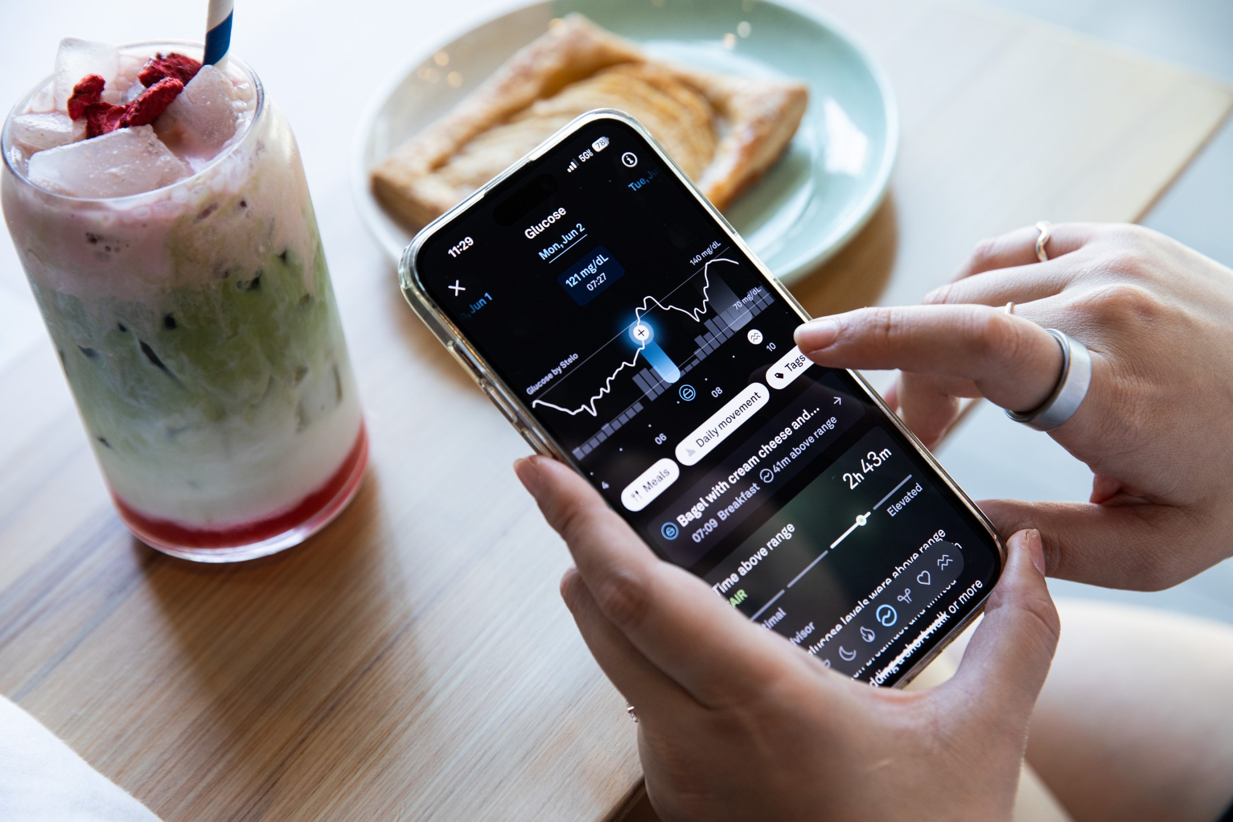 Person looking at their glucose levels in the Oura app with a strawberry matcha latte and a pastry in the background.