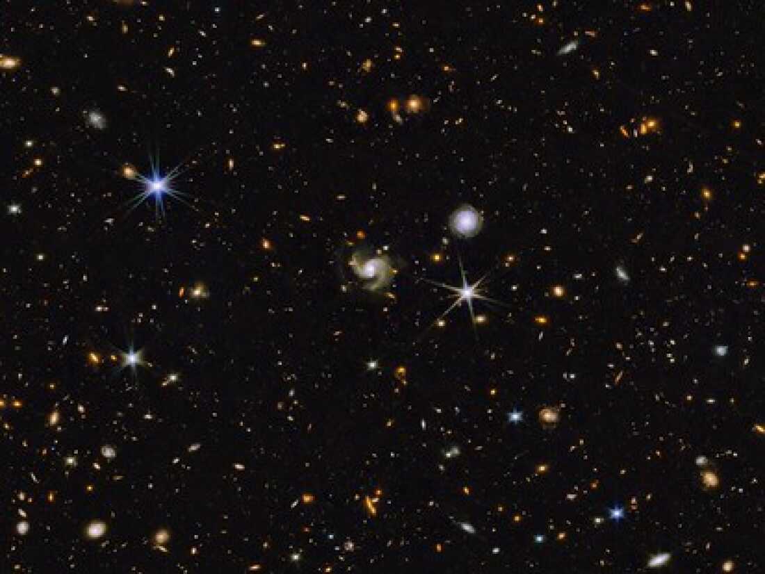 This multi-wavelength image from NASA shows a universe full of galaxies that are various shapes, colors and sizes. Most are small while a handful are somewhat larger. A few stars are also scattered across the image. 
