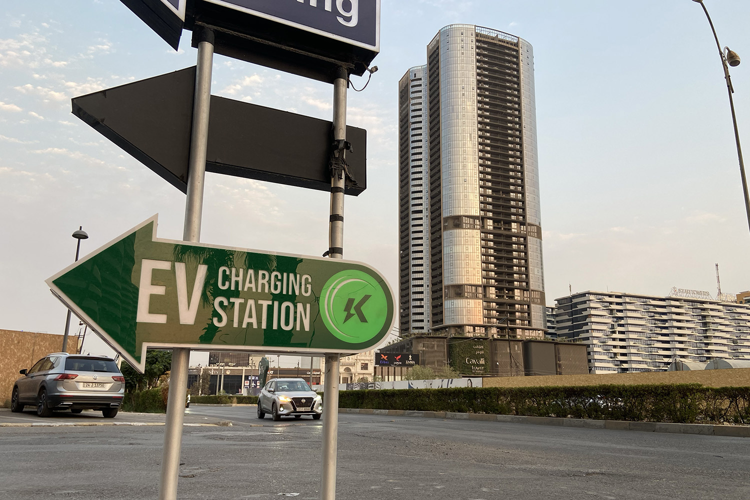 Signs reading "Parking" and "EV charging station" in English stand in front of cars and a high-rise building.