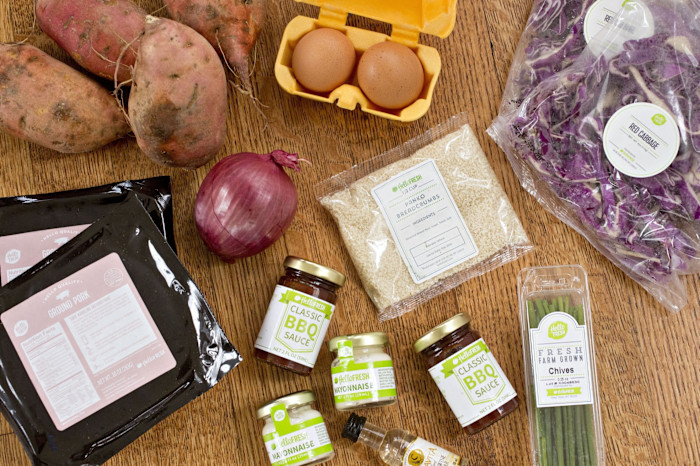 A variety of ingredients from a HelloFresh meal kit are displayed on a wooden surface