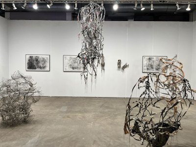 Several intricate sculptures made from electrical wire and silk organza hang in the center of an art fair booth.