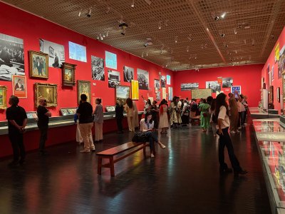 Installation view of a museum gallery with red painted walls showing various objects on the walls and in vitrines.