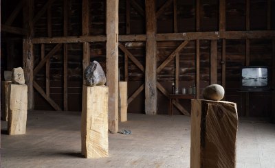 Various rocks on wooden plinths in a barn, with a TV in the background.