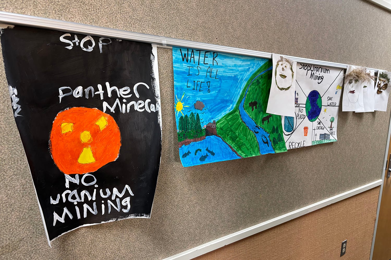 Handmade signs hang on a bulletin board. They read: "Stop: Panther mineral; No uranium mining" and "WATER IS ALL LIFE!"