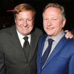 Two men in suits smile for the camera.